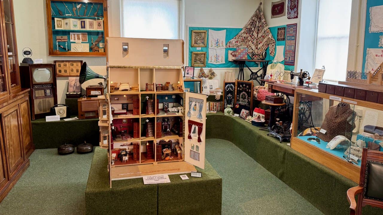 The Holgate family dolls' house at Nidderdale Museum, surrounded by curling stones, an early television, a gramophone, sewing machines and embroidery.