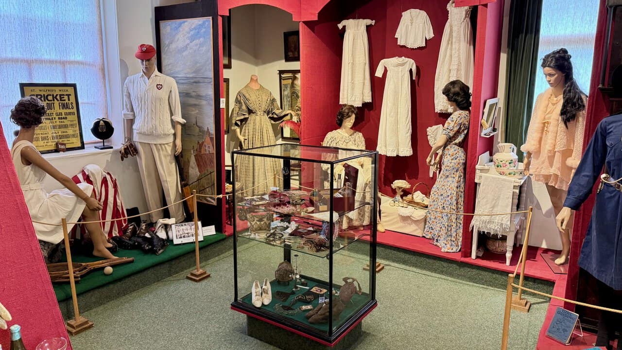 Mannequins in the Costume Room dressed in cricket whites, period dresses and nightwear, with christening gowns hanging behind.