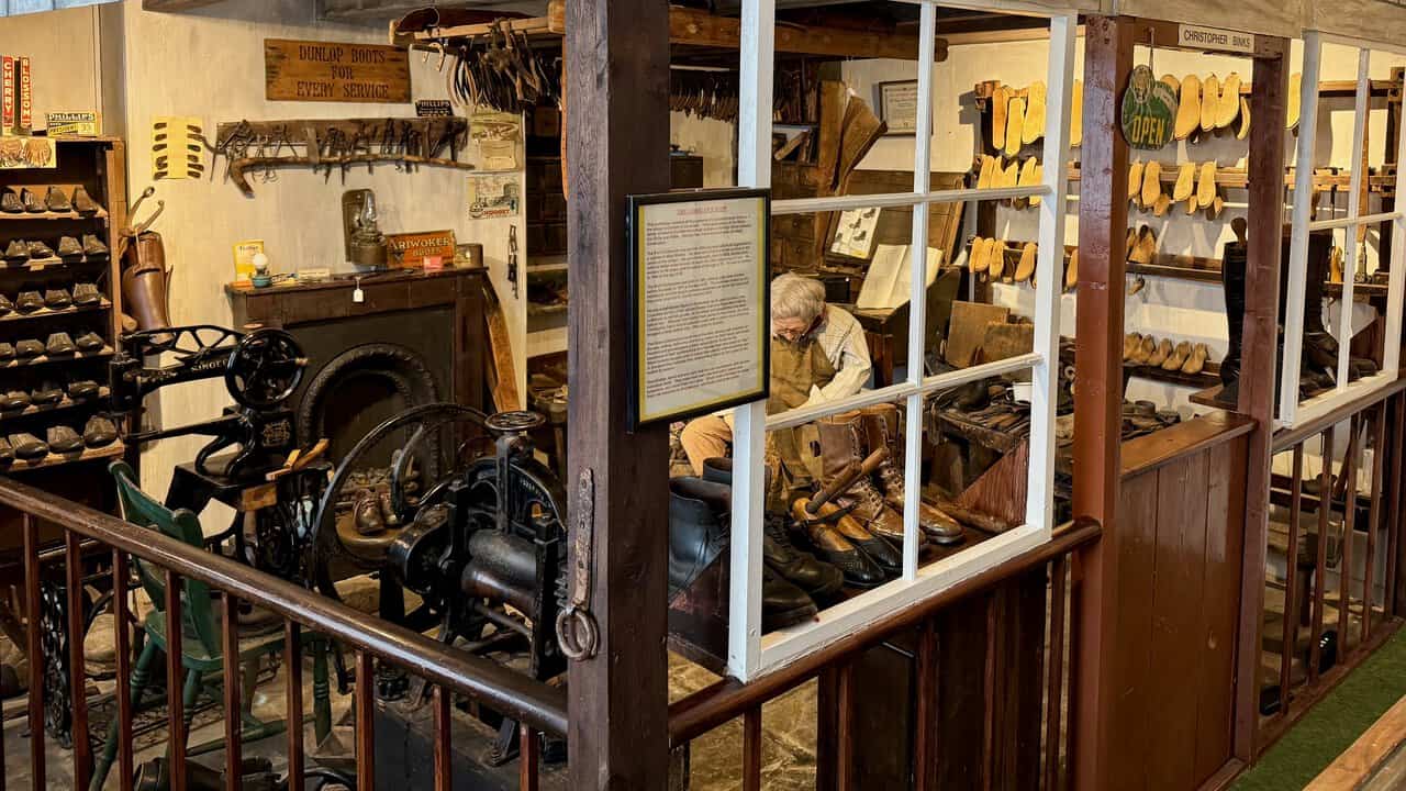 Christopher Binks at his cobbler's bench, surrounded by racks of wooden lasts, a stitching machine and an old Dunlop boots sign.