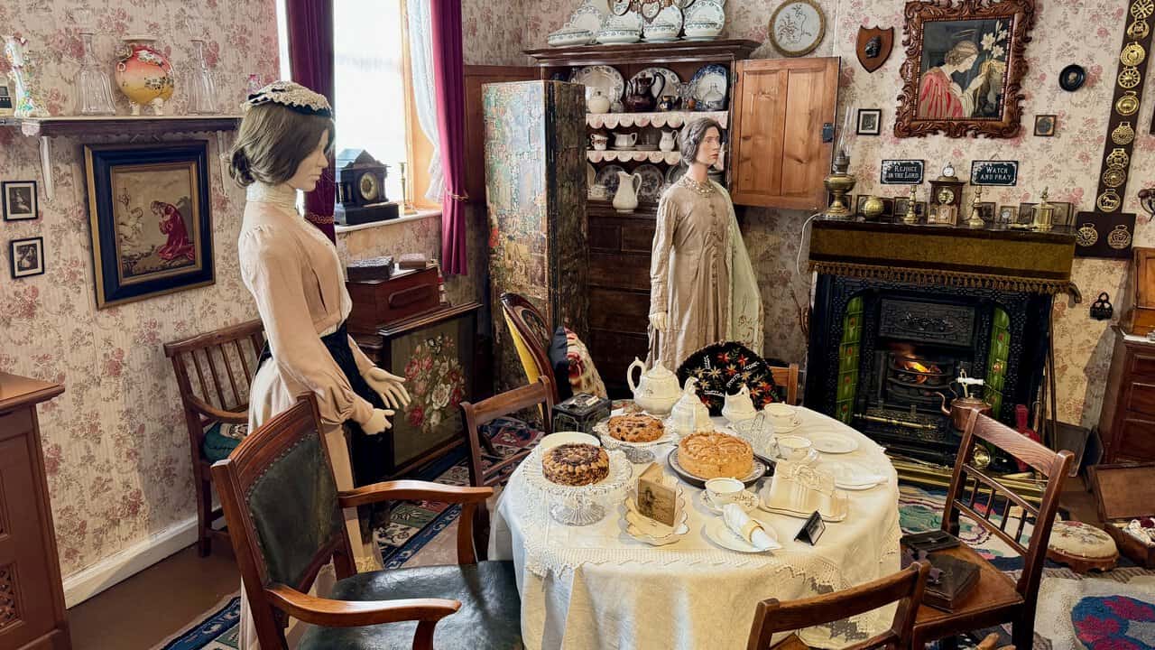 A recreated Victorian parlour, with afternoon tea laid by the fireplace, framed religious texts on the wall and a dresser full of china.