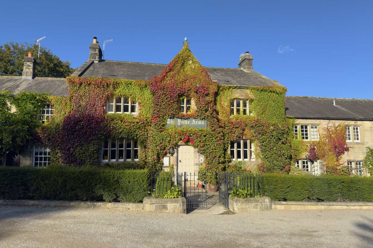 The stone-built Yorke Arms in Ramsgill, its front covered in red and green creeper, behind neat hedges and iron gates.